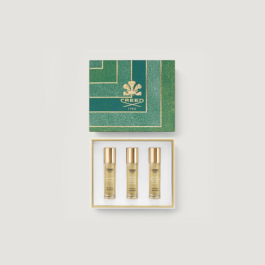 Three Creed perfume bottles in a gold and green box on a grey background