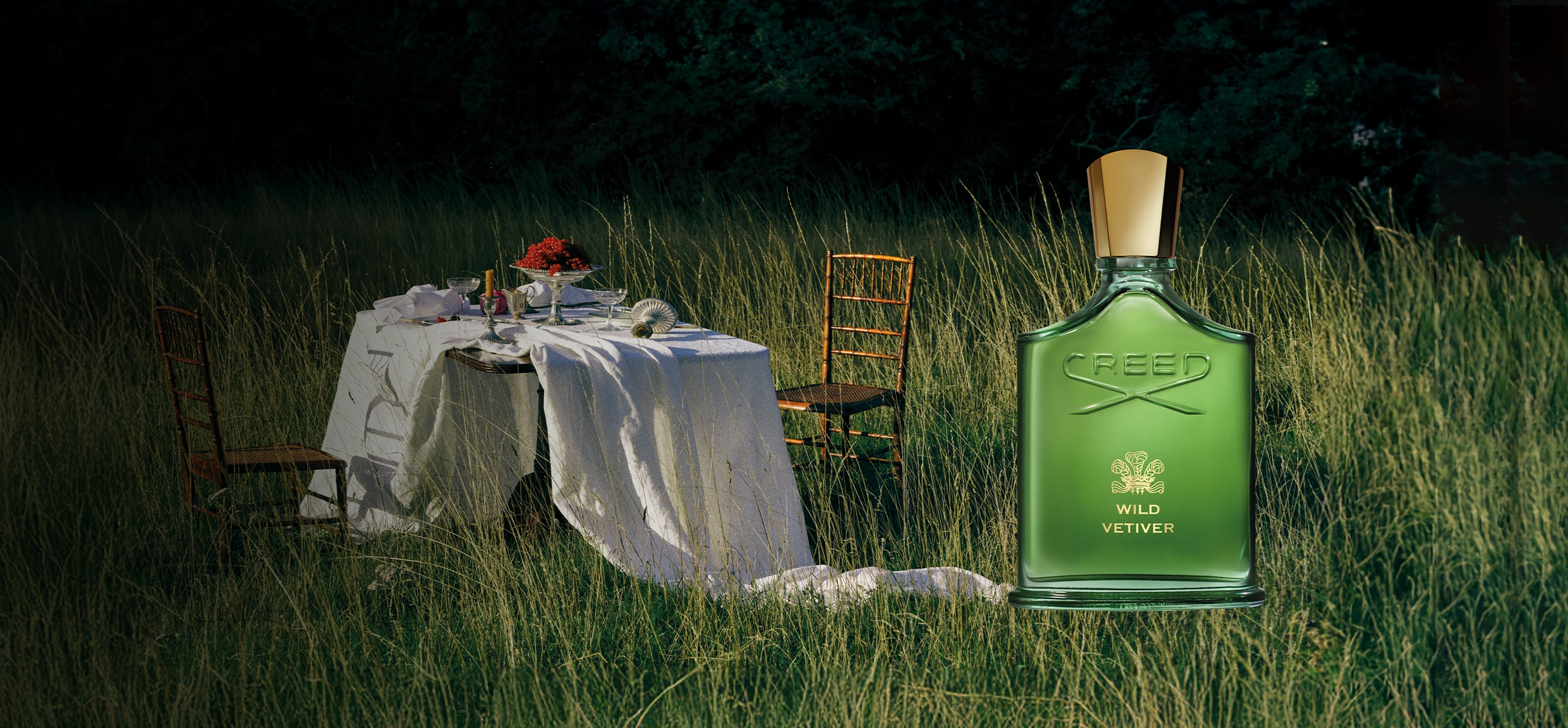 Green bottle of Ciroc Vodka in a grassy outdoor setting with a table and chairs.