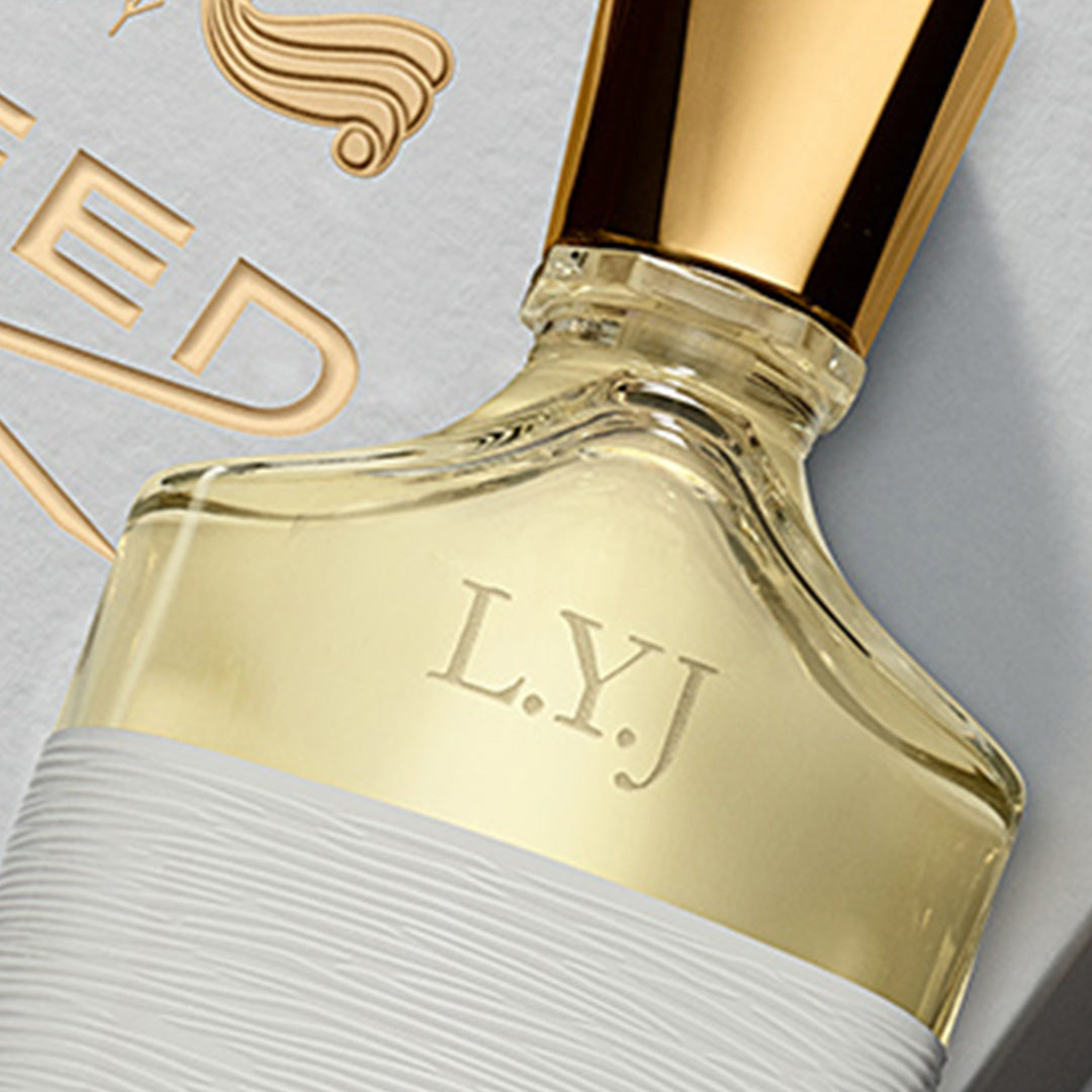 Close-up of a perfume bottle with gold cap and 'L.Y.J.' engraving on a light gray background.