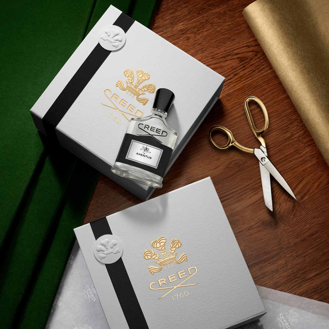 Creed perfume bottle and packaging on a wooden surface with gold scissors.