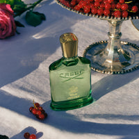 Green Creed perfume bottle on a white surface with red berries and a pink rose.